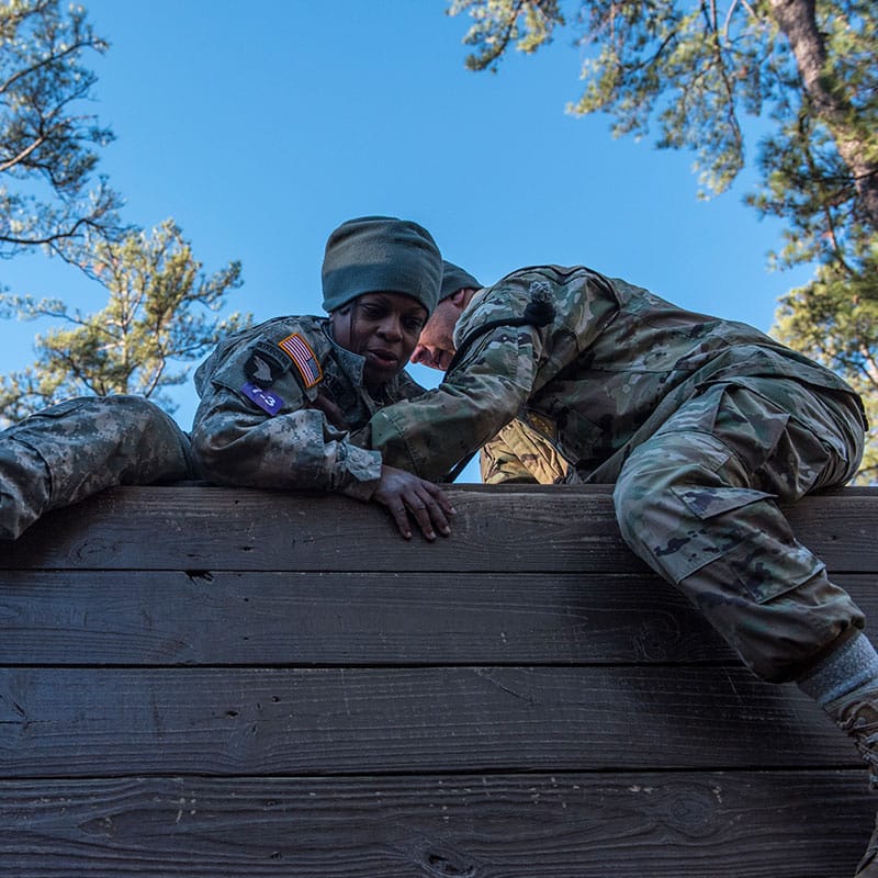 diers help a fellow soldier over a wall on an obstacle course